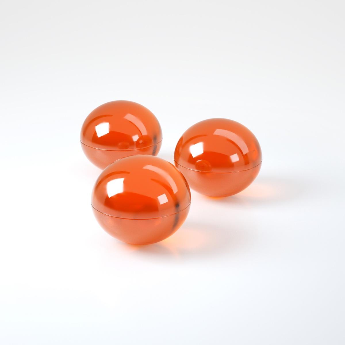 Studio product shot displaying three translucent orange oil spheres grouped together on a white reflective surface.