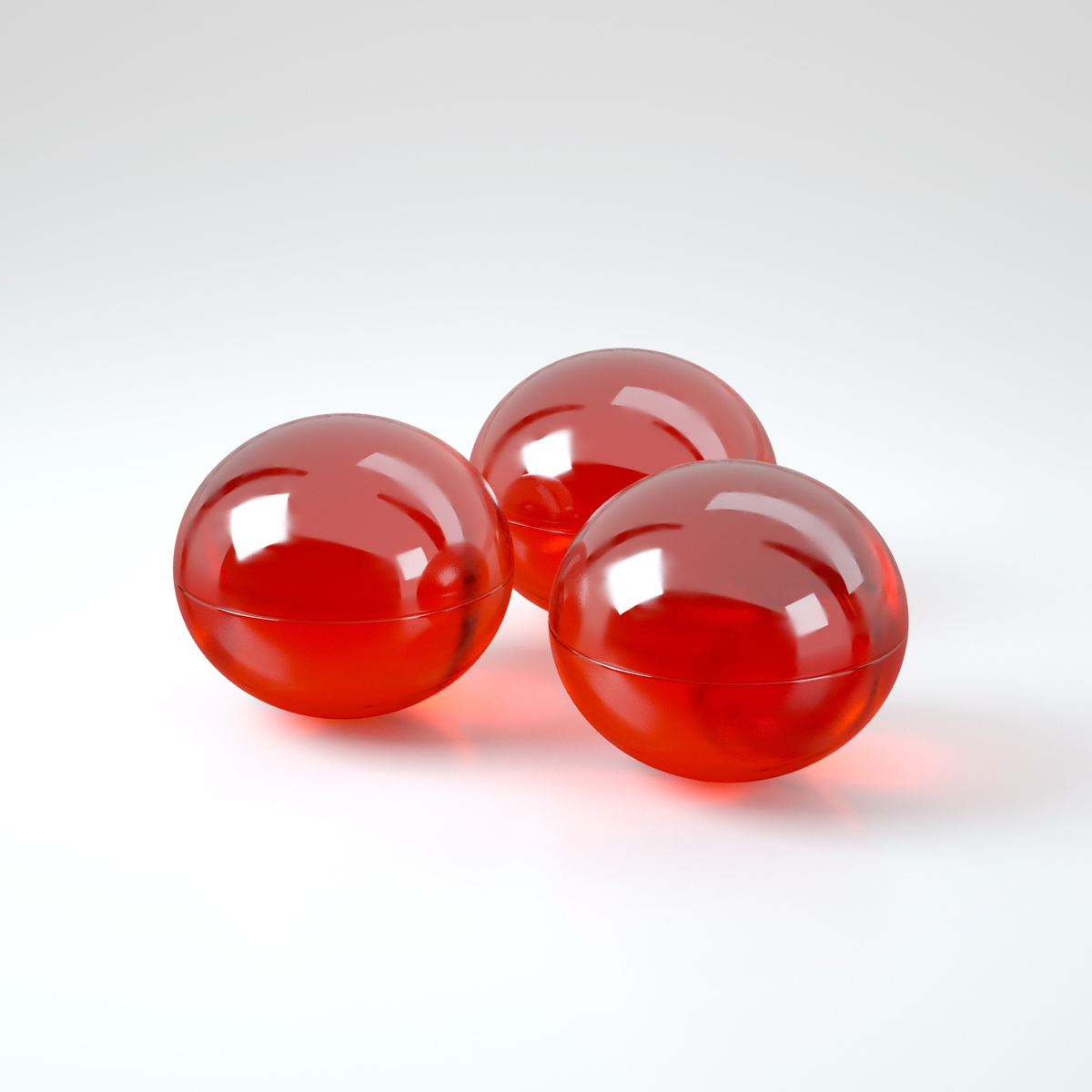 Studio product shot displaying three translucent red oil spheres grouped together on a white reflective surface.