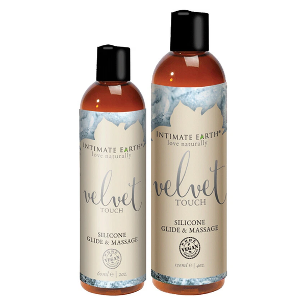 Size comparison view showing two amber bottles of Intimate Earth Velvet Touch silicone glide and massage oil standing side by side in 60 ml (2 fl oz) and 120 ml (4 fl oz) capacities.