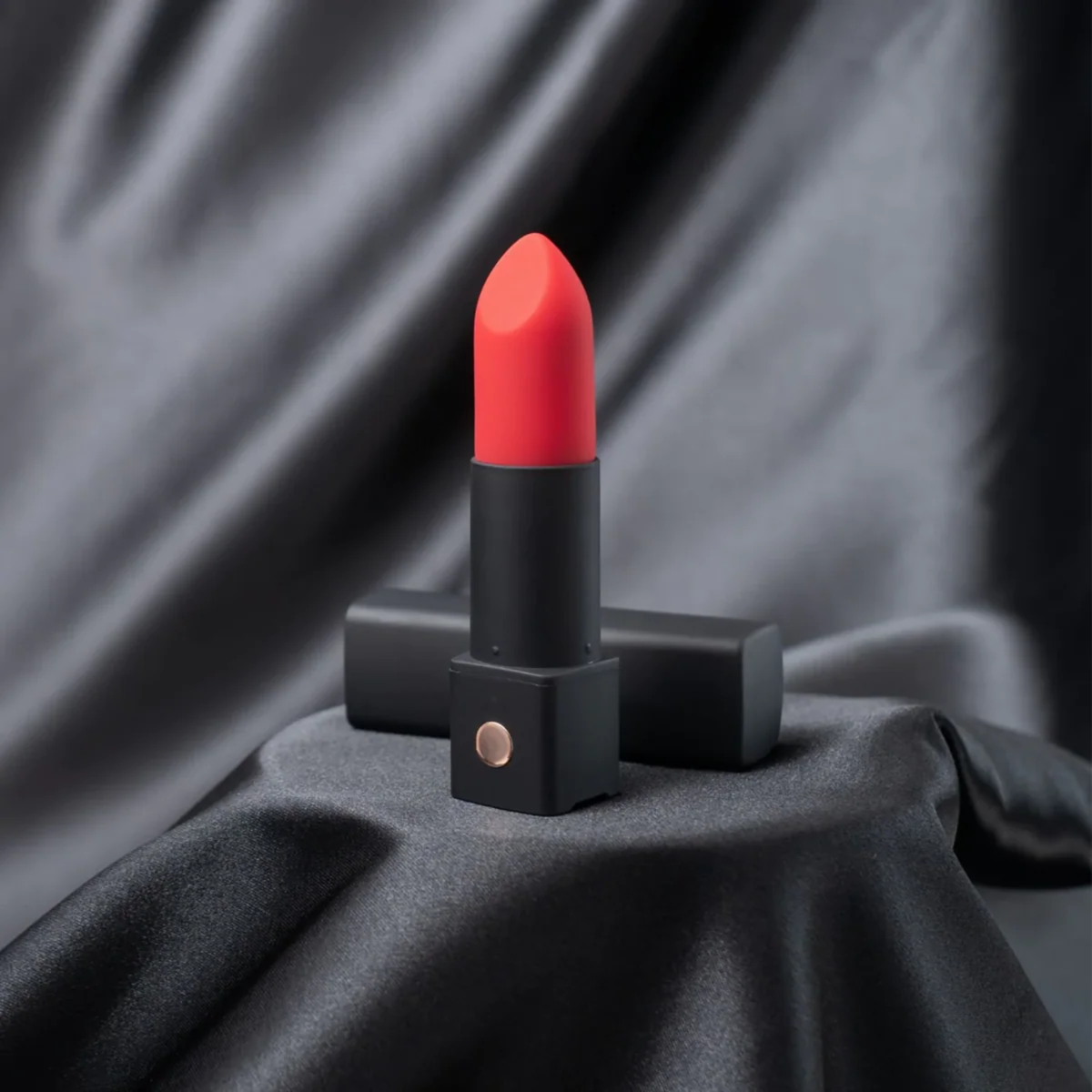 Studio display photo of the open Lovense Exomoon lipstick vibrator standing in front of its cap on a draped black satin background.