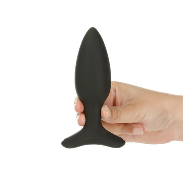 Scale perspective photo showing a hand holding the small black Lovense Hush 2 vibrating butt plug by its neck.