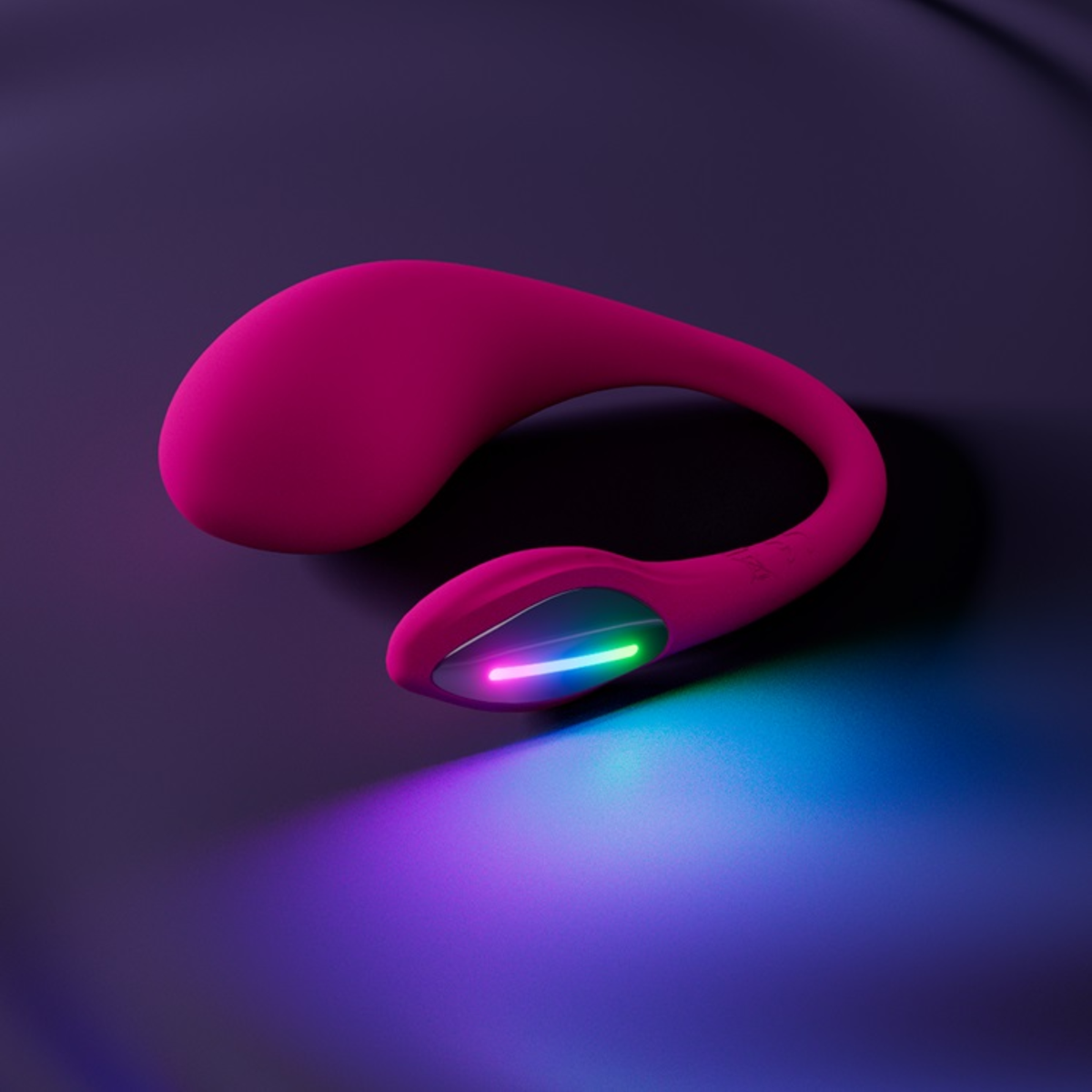 Mood shot of the pink Lovense Lush 4 resting on a dark purple surface with its LED tip casting a vibrant blue and pink glow.