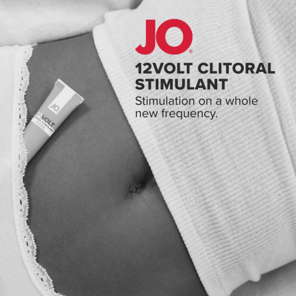 A close-up, cropped black and white photo of a person's stomach, with the System JO 12VOLT tube tucked into the waistband of their underwear. The red System JO logo and product name are printed on the right.