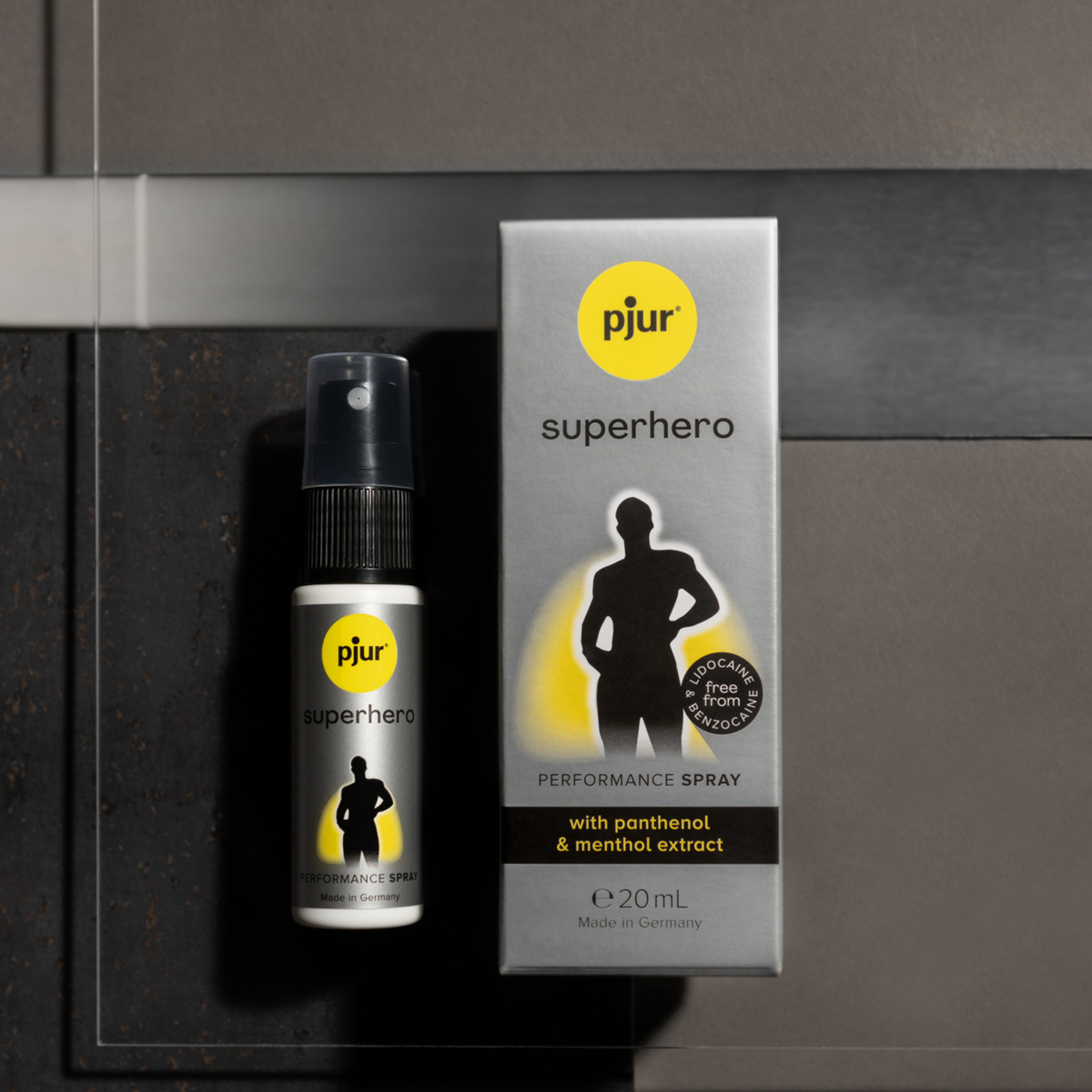 A gray box and white spray bottle of Pjur Superhero Performance Spray are shown against a blurred background.