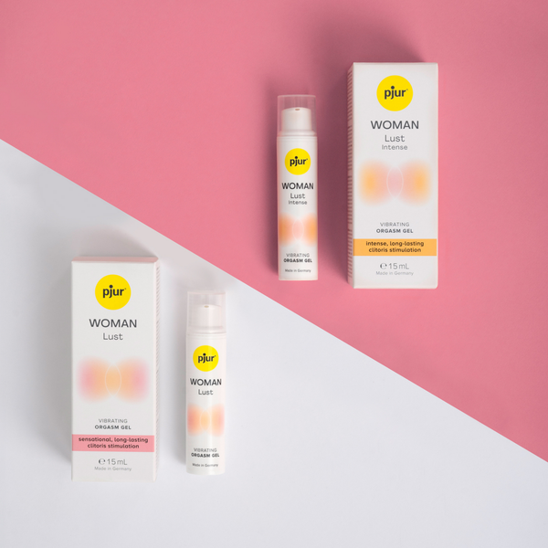 Two white boxes and two matching white tubes of Pjur Woman Lust orgasm gel are arranged on a diagonally split background of white and pink.